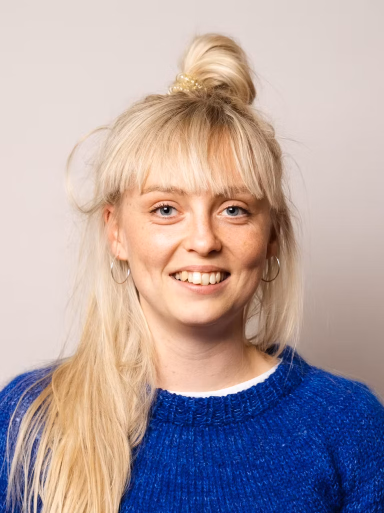 Fie Dandanell, journalist, smiling in a portrait photo wearing a blue knitted sweater